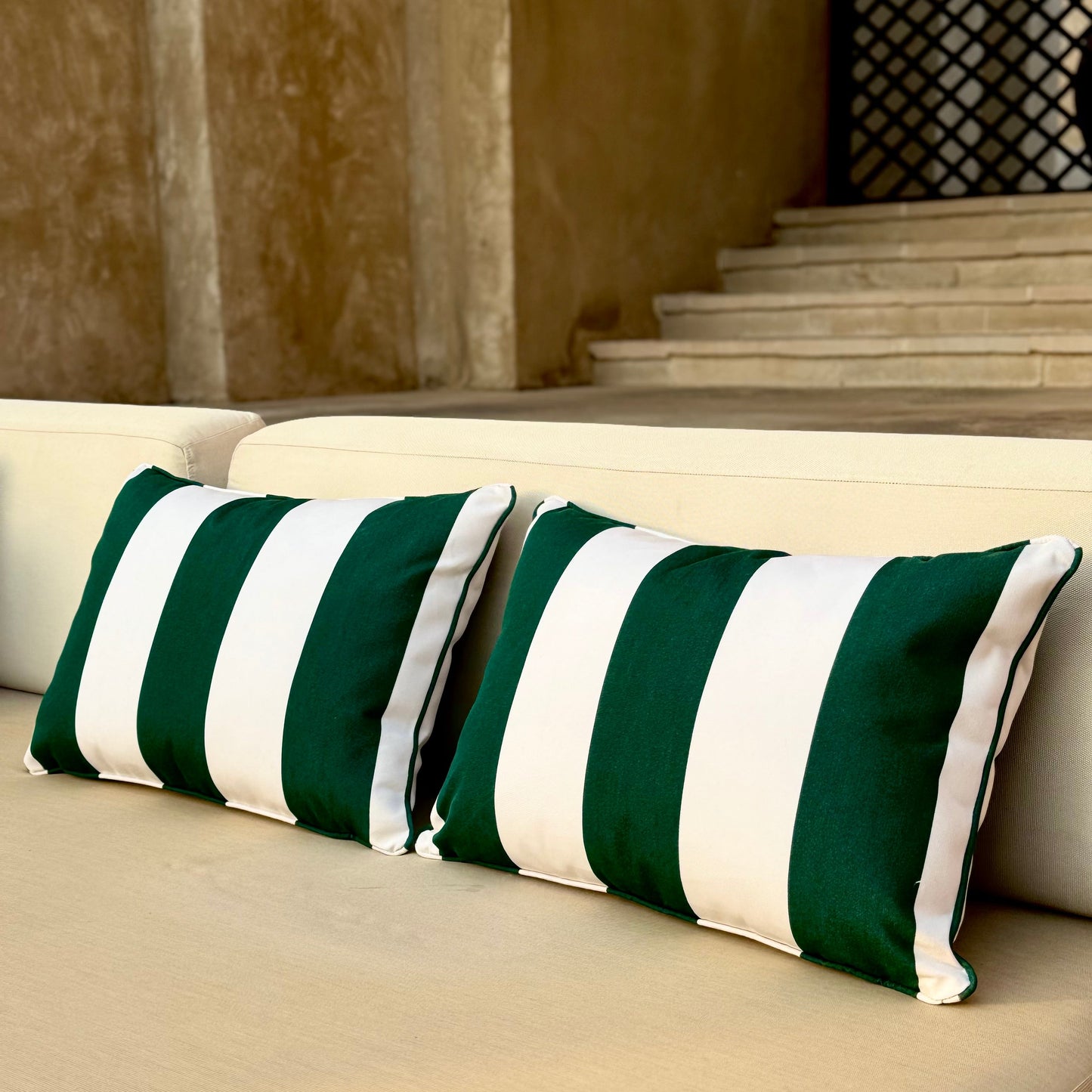 Green and white striped pillows on a beige outdoor sofa with a stone wall background.
