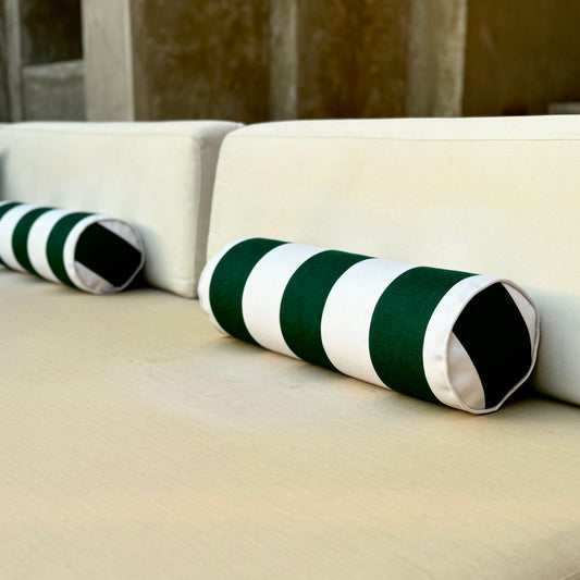 Beige sofa with green and white striped cushions against a stone wall.