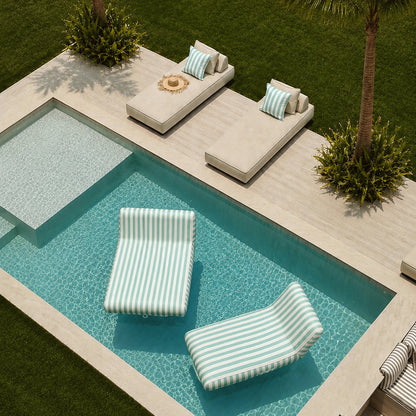 Modern outdoor poolside scene with a rectangular swimming pool, two striped lounge chairs in the water, two matching lounge chairs on the deck, palm trees, green lawn, and a clean architectural setting.