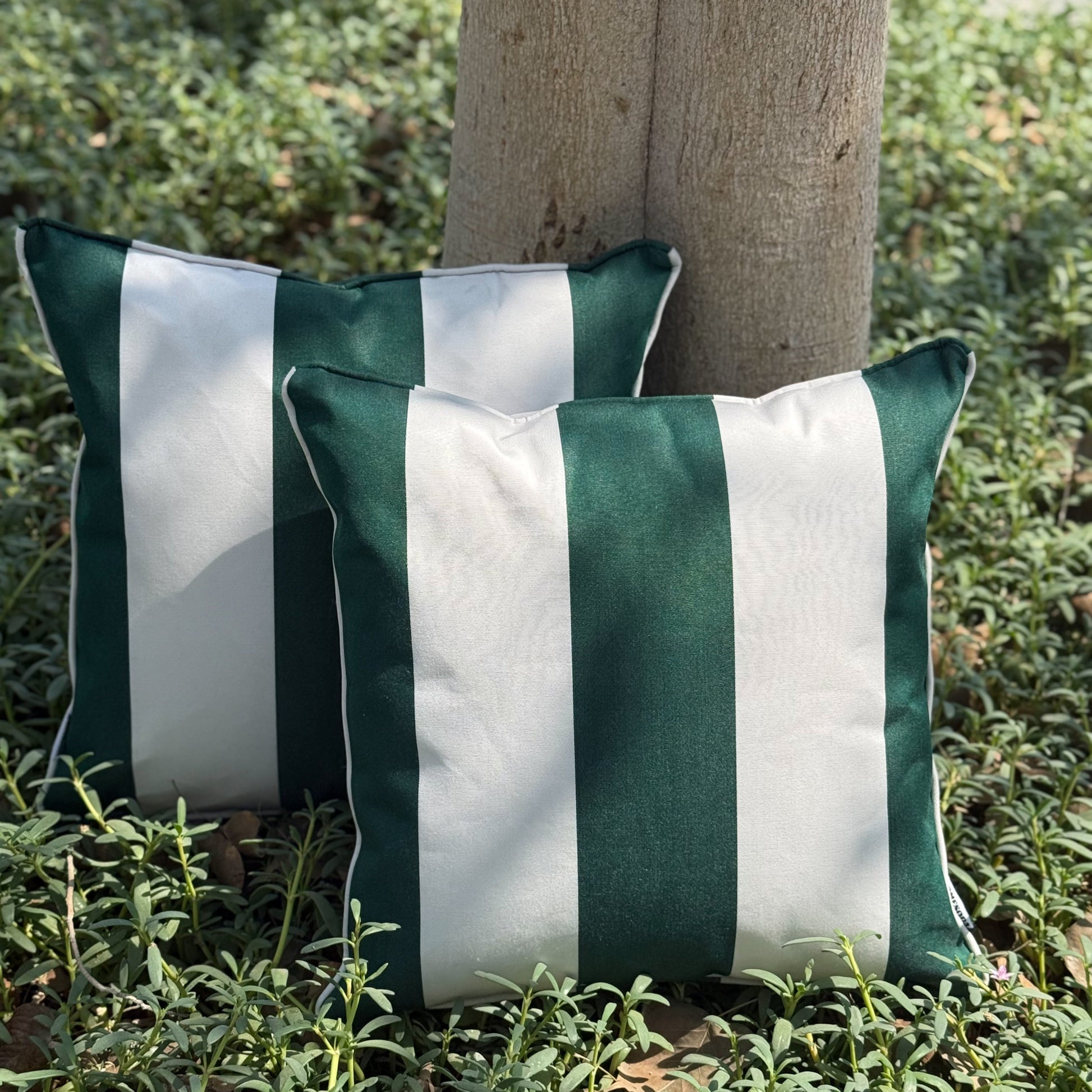 Two green and white striped pillows on a grassy surface.