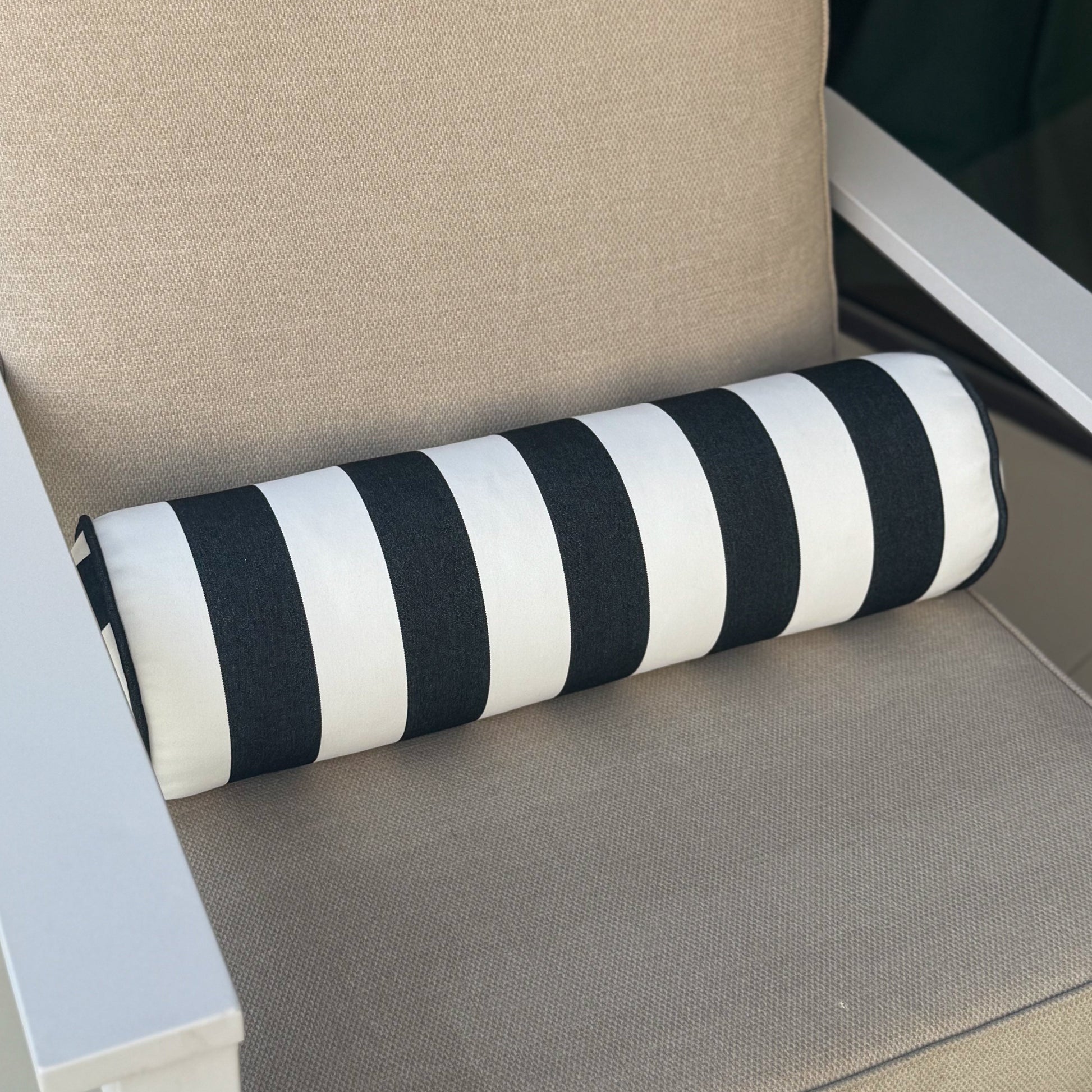 Chair with beige cushion and black and white striped cylindrical pillow