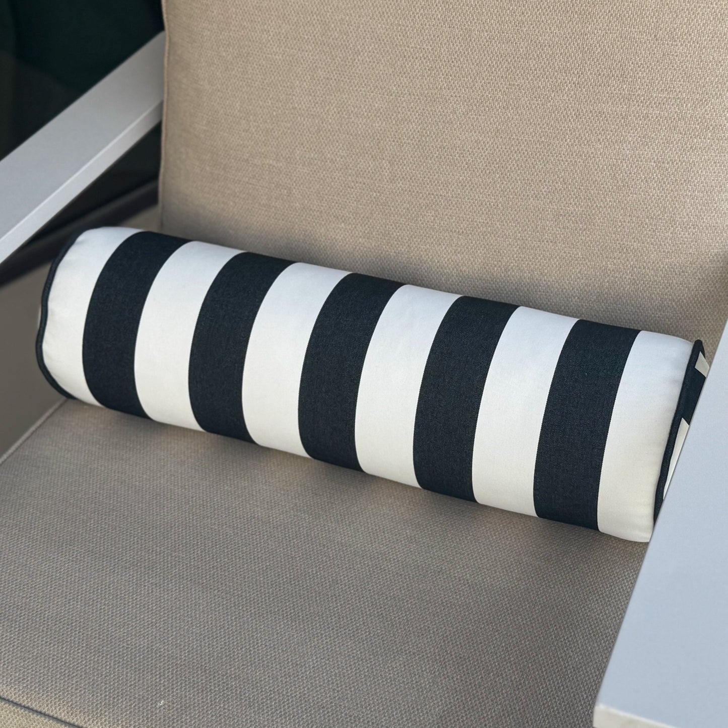 Chair with beige cushion and black and white striped bolster pillow on a neutral background