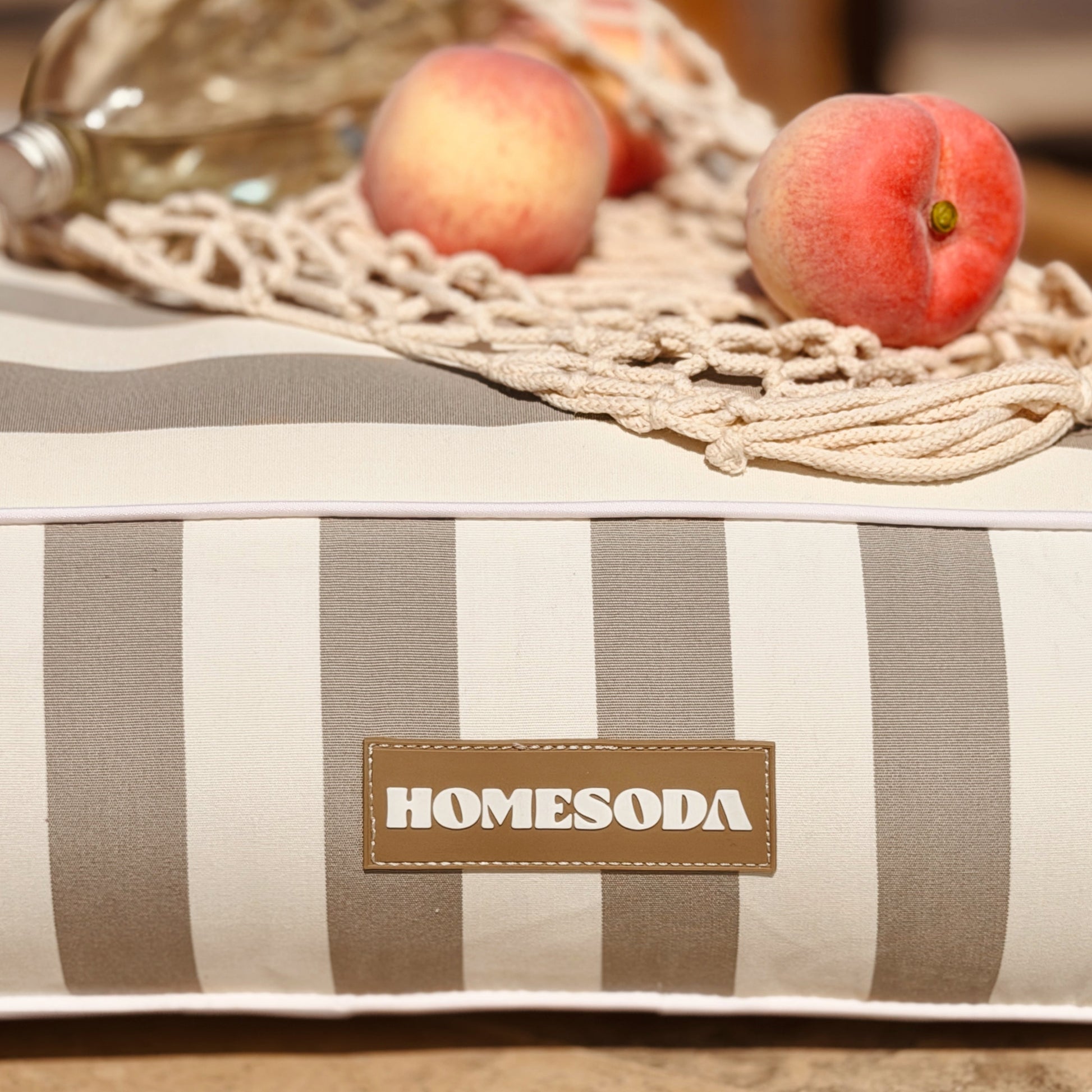 Striped cushion with 'HOMESODA' label on a surface with peaches and a basket.
